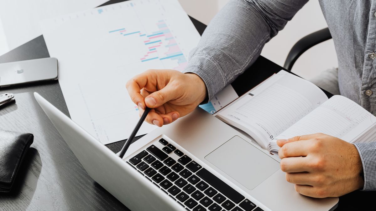 Professional using laptop and reviewing documents at office desk for data analysis.