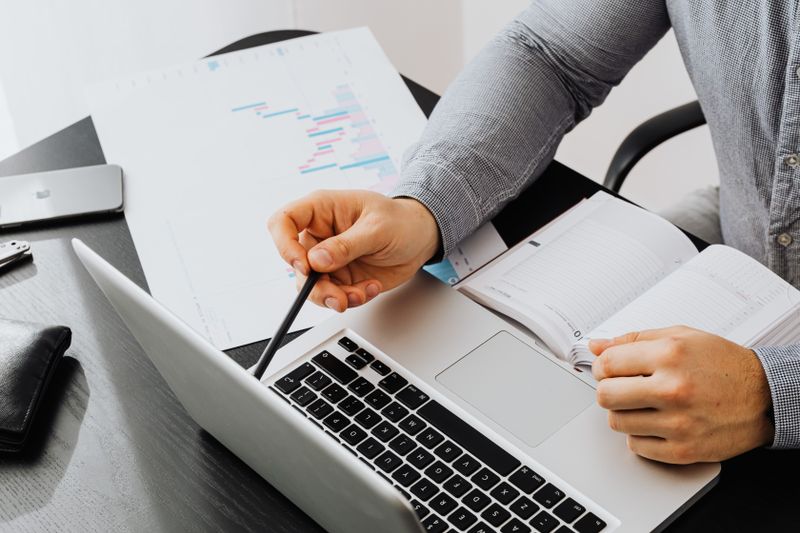 Professional using laptop and reviewing documents at office desk for data analysis.