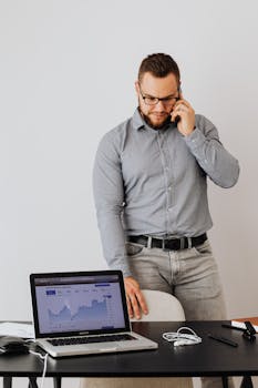 Businessman talking on phone while viewing data graphs on laptop indoors.