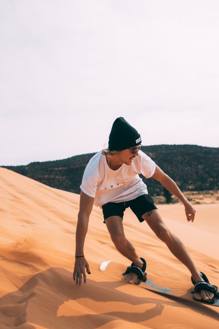 A man sandboarding down a sunny desert dune in Utah, embracing nature and adventure.