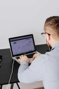 A man uses a laptop indoors to analyze stock market trends graph on screen.