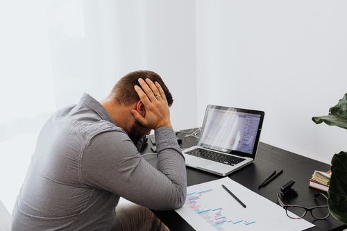 Free A man looking stressed at his desk, hands on head, with a laptop and graphs. Stock Photo
