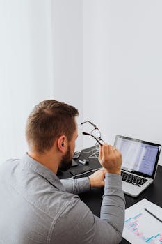 A man in gray attire reviews analytical graphs on a laptop, showcasing focused work in an office setting.