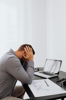 一个沮丧的人坐在办公桌前，面前摆着笔记本电脑和图表，显示出工作压力