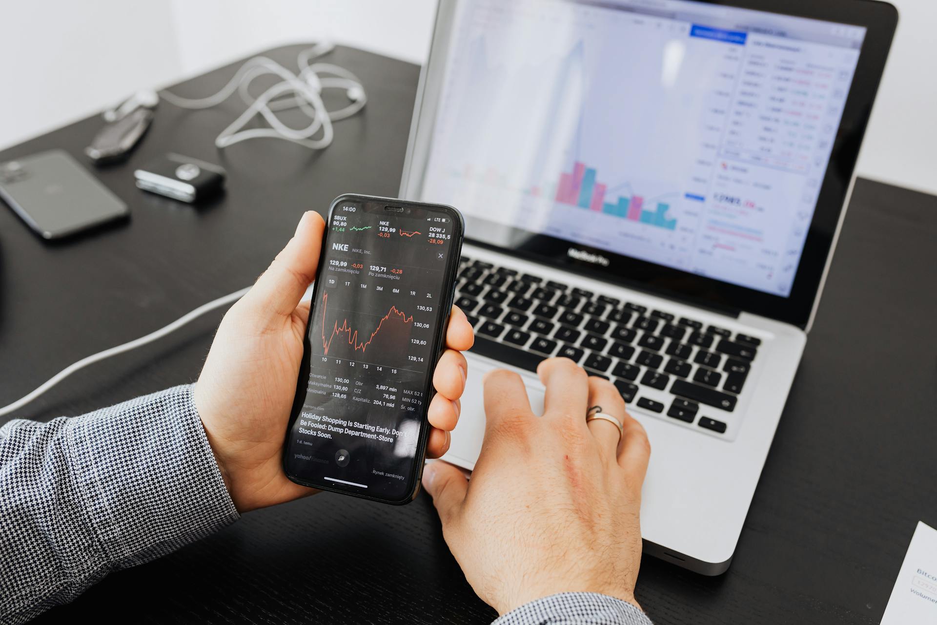 Person analyzes stock data with a smartphone and laptop, indoors.