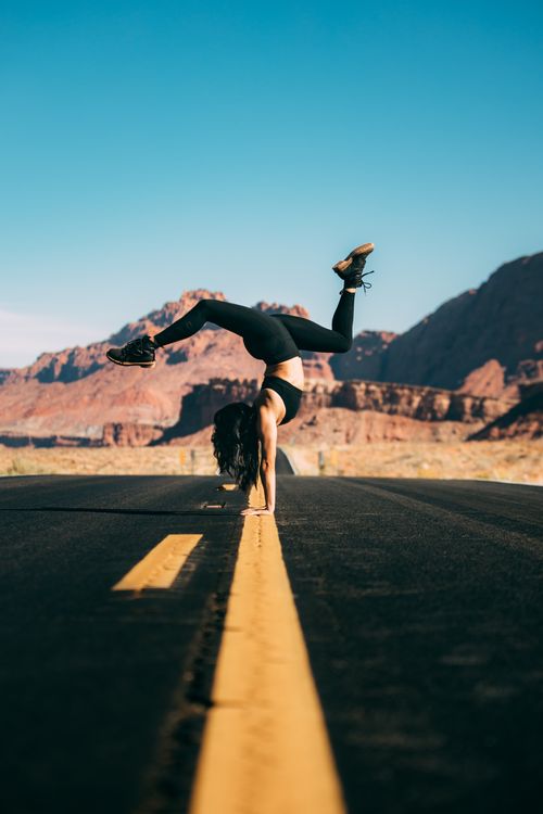 Free Woman in sportswear doing a handstand on a desert road against a blue sky. Stock Photo