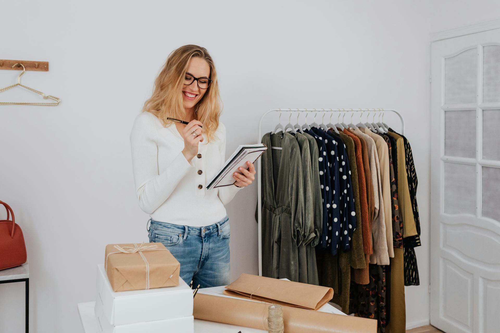 Businesswoman taking inventory in a clothing store, smiling while writing notes.