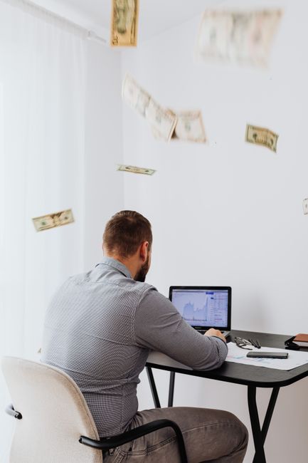 A man sits at a desk with a laptop and floating currency, symbolizing financial growth. A man sits at a desk with a laptop and floating currency, symbolizing financial growth.