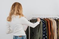 Woman in White Long Sleeve Shirt and Blue Denim Jeans Standing in Front of Clothes