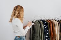 女人在室内检查服装架，并写下笔记，架上装有各种时尚服装