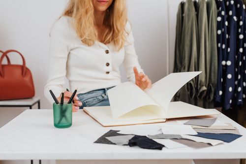 Free A woman analyzes fabric samples in a fashion studio setting, surrounded by designs and materials. Stock Photo