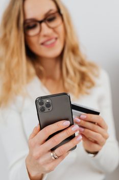 高加索女人拿着智能手机和信用卡，微笑着在网上购物