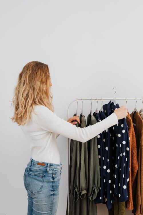 Free A woman with blond hair selecting clothes from a clothes rack indoors. Stock Photo