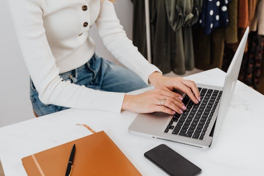 A woman in a white sweater typing on a laptop in a stylish office environment.