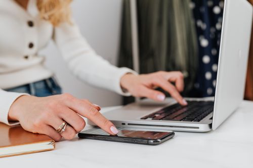 Free Close-up of a woman's hands using a laptop and smartphone simultaneously on a desk. Stock Photo