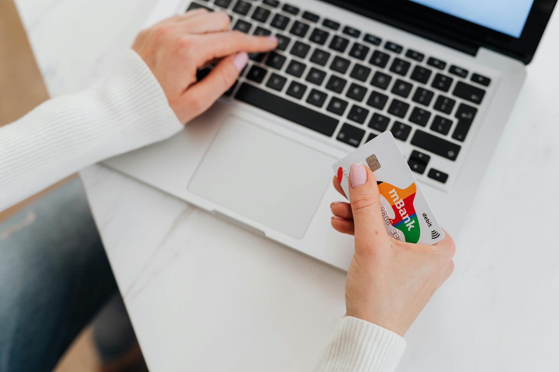 Close-up of a person using a laptop and holding a credit card for online shopping.