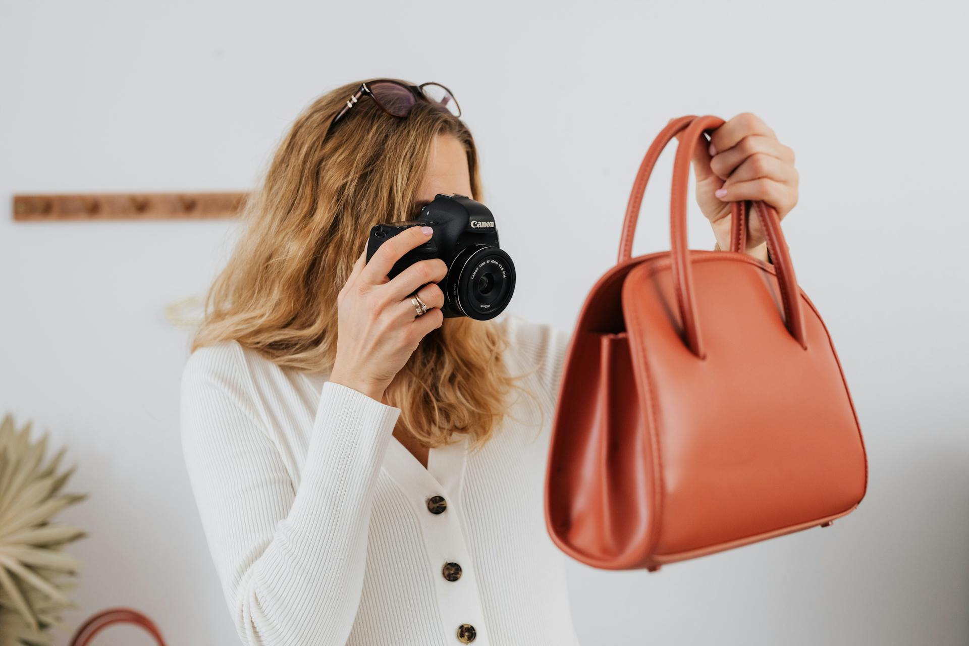 A woman in white long sleeves photographs a handbag, ideal for online selling and fashion themes.