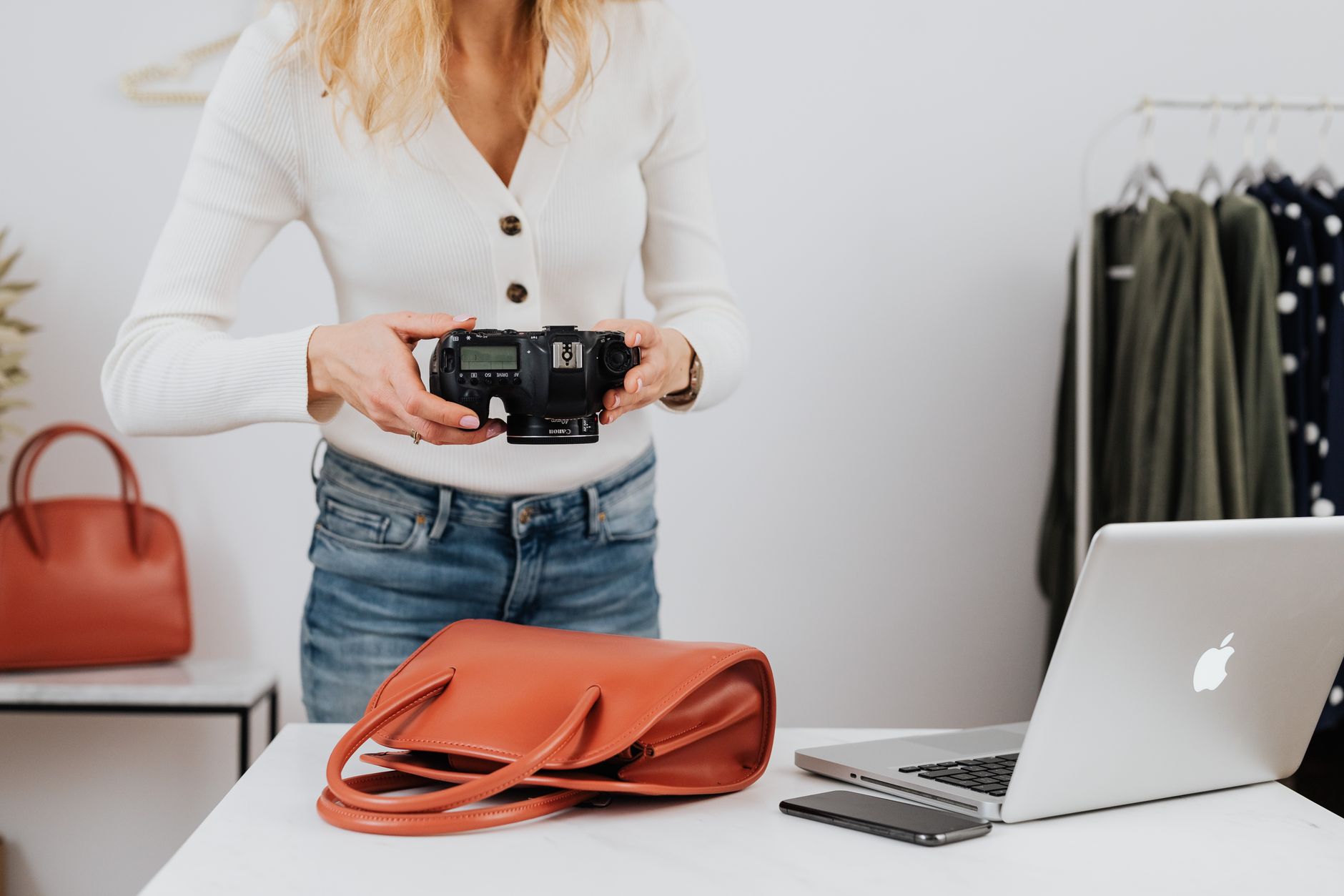 Femme photographiant des articles de mode à l'intérieur avec un DSLR, un sac à main et un ordinateur portable.