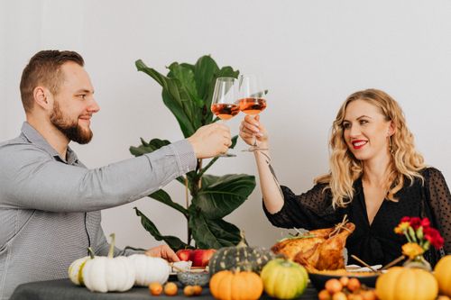 Free A couple toasting with rosé wine over a festive Thanksgiving dinner with pumpkins and turkey. Stock Photo