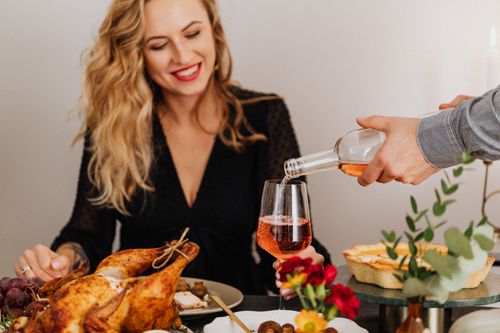 Free A joyful festive dinner with a smiling woman having wine poured, enhancing the holiday spirit. Stock Photo