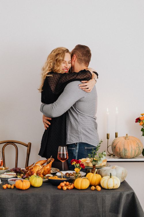 Free A joyful couple hugging in a thanksgiving setting with a richly decorated dinner table. Stock Photo