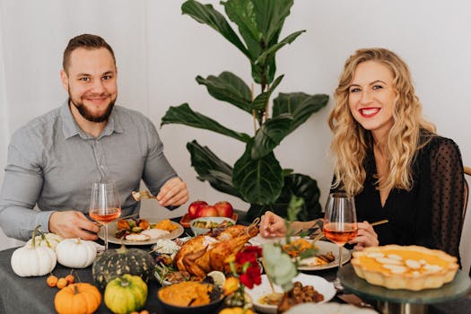 A cheerful couple enjoys a festive autumn dinner with roasted chicken, pumpkin pie, and wine indoors.