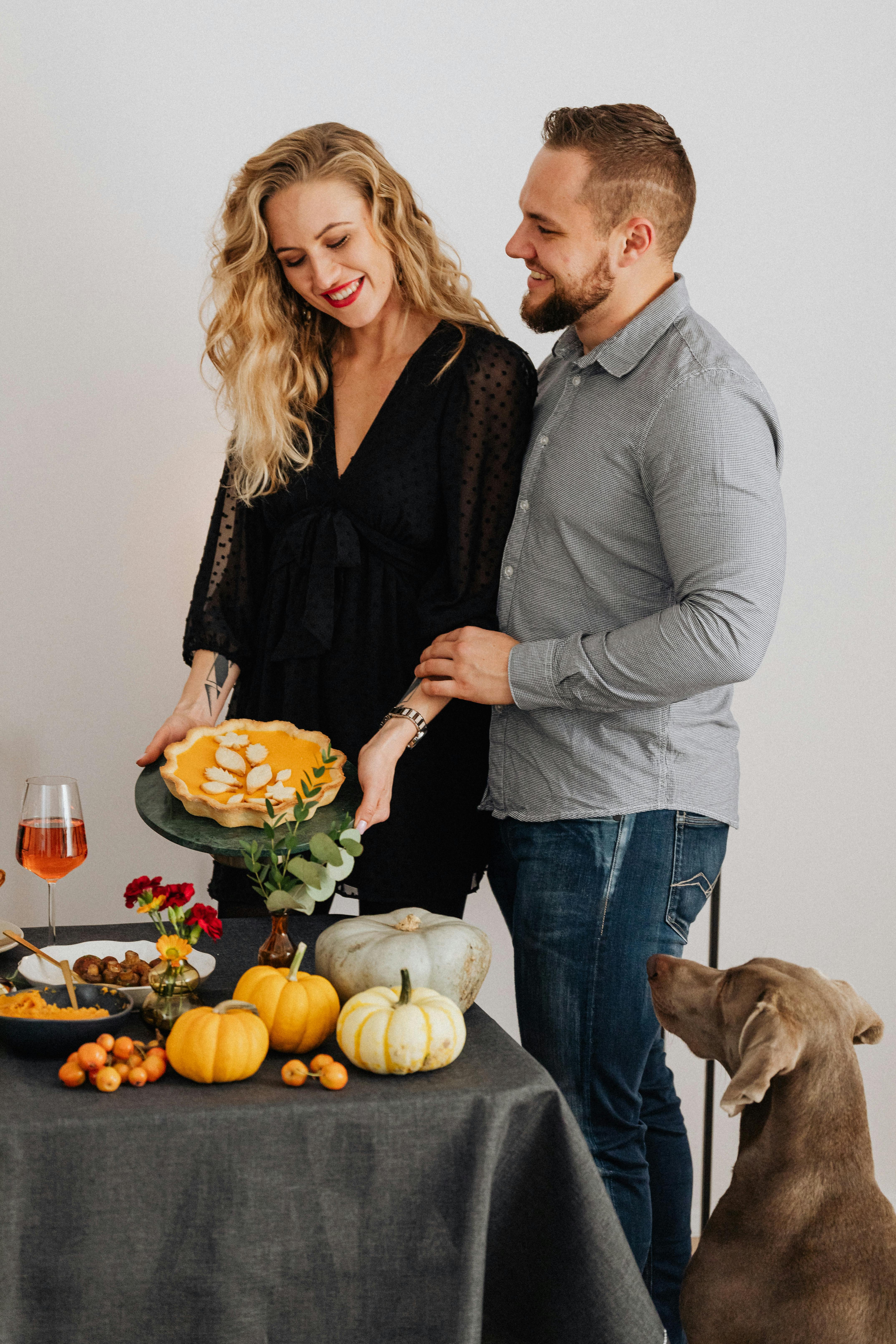 一对快乐的夫妇为感恩节晚餐用南瓜和威玛狗装饰桌子