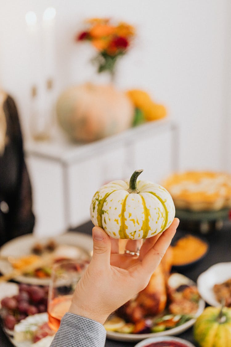 Hand Holding Small Pumpkin And Dinner Table In Background