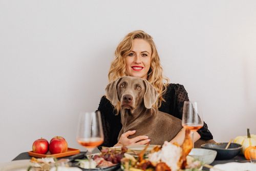 Free A smiling woman holding her dog at a cozy dinner table setting, enjoying a festive atmosphere. Stock Photo