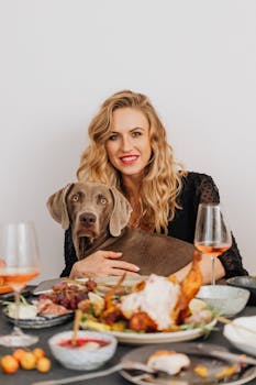 Blonde woman and Weimaraner dog at a festive dinner table.