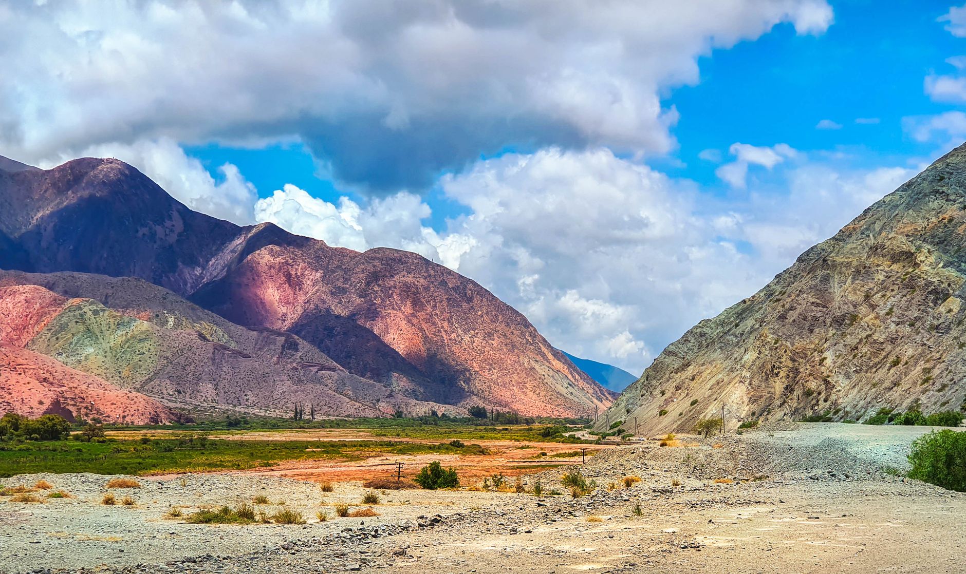Vibrant panoramic view of multicolored mountains under a dramatic blue sky with clouds.