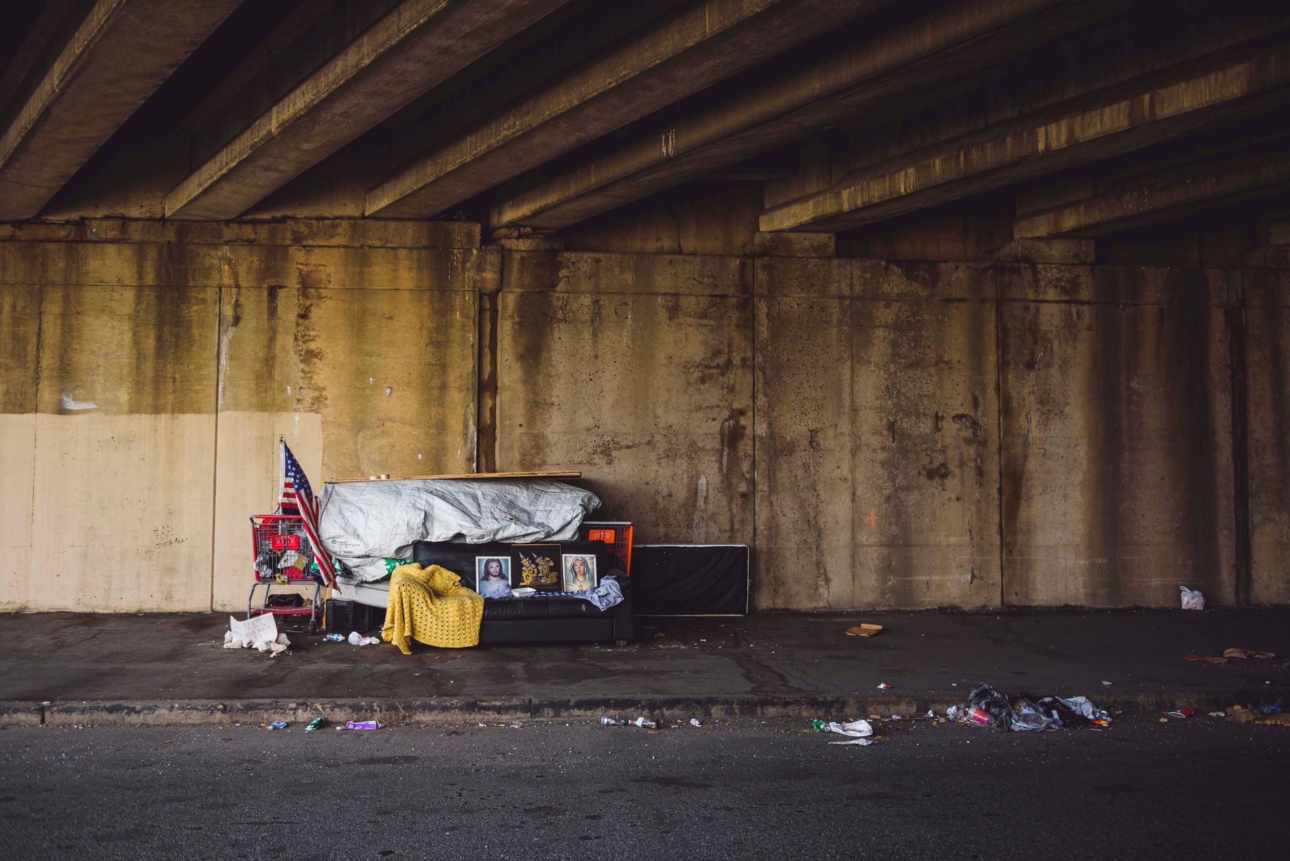 A gritty urban underpass in Philadelphia with signs of homelessness and American flag.