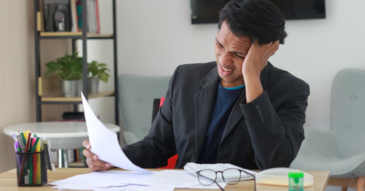 Hispanic man reviewing auto insurance documents at a Texas kitchen table, frustrated expression