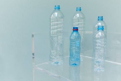 Free Five assorted empty plastic bottles displayed on a clear shelf with a soft blue background. Stock Photo