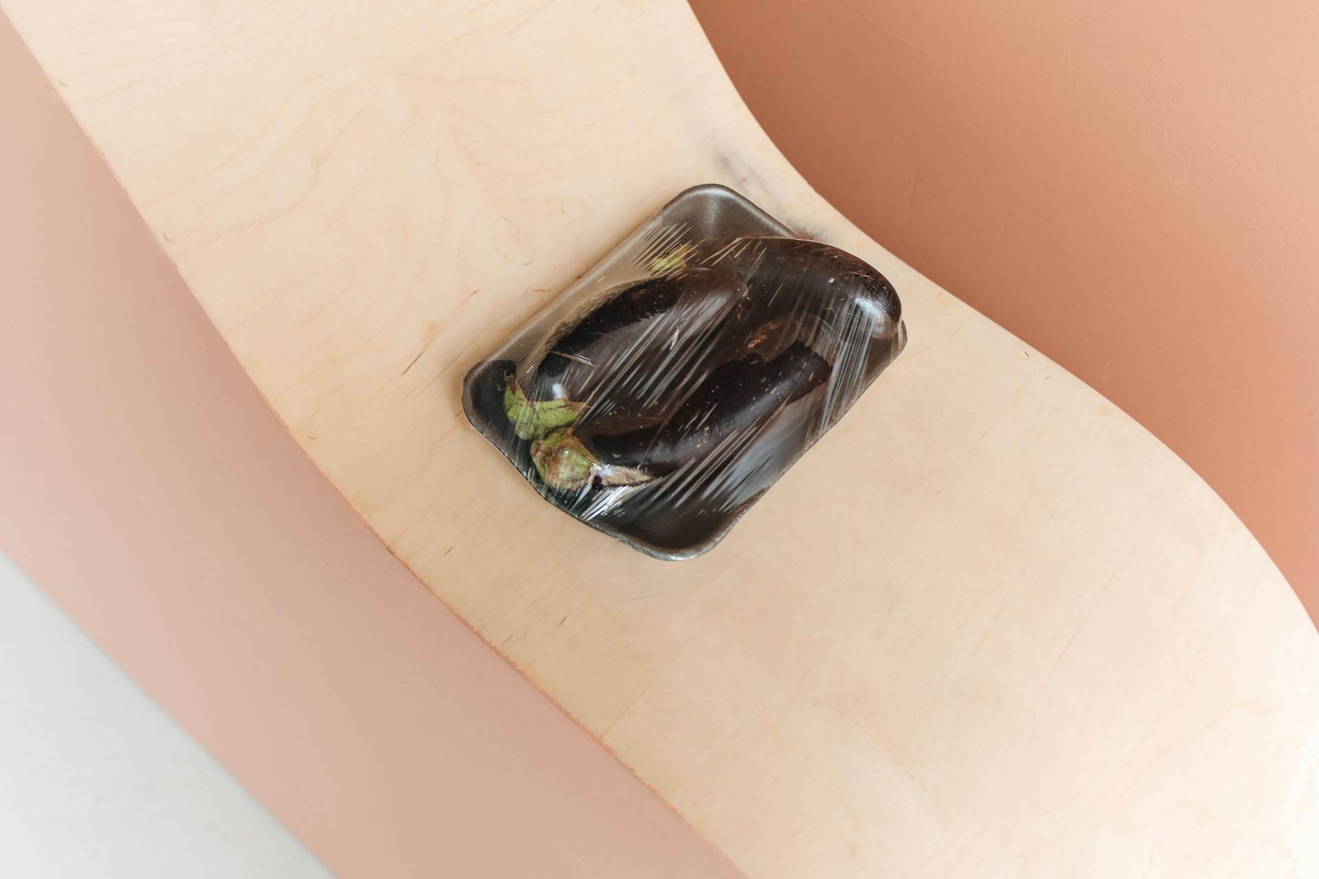 Close-up of fresh eggplants wrapped in plastic on a wooden shelf, emphasizing zero waste concepts.