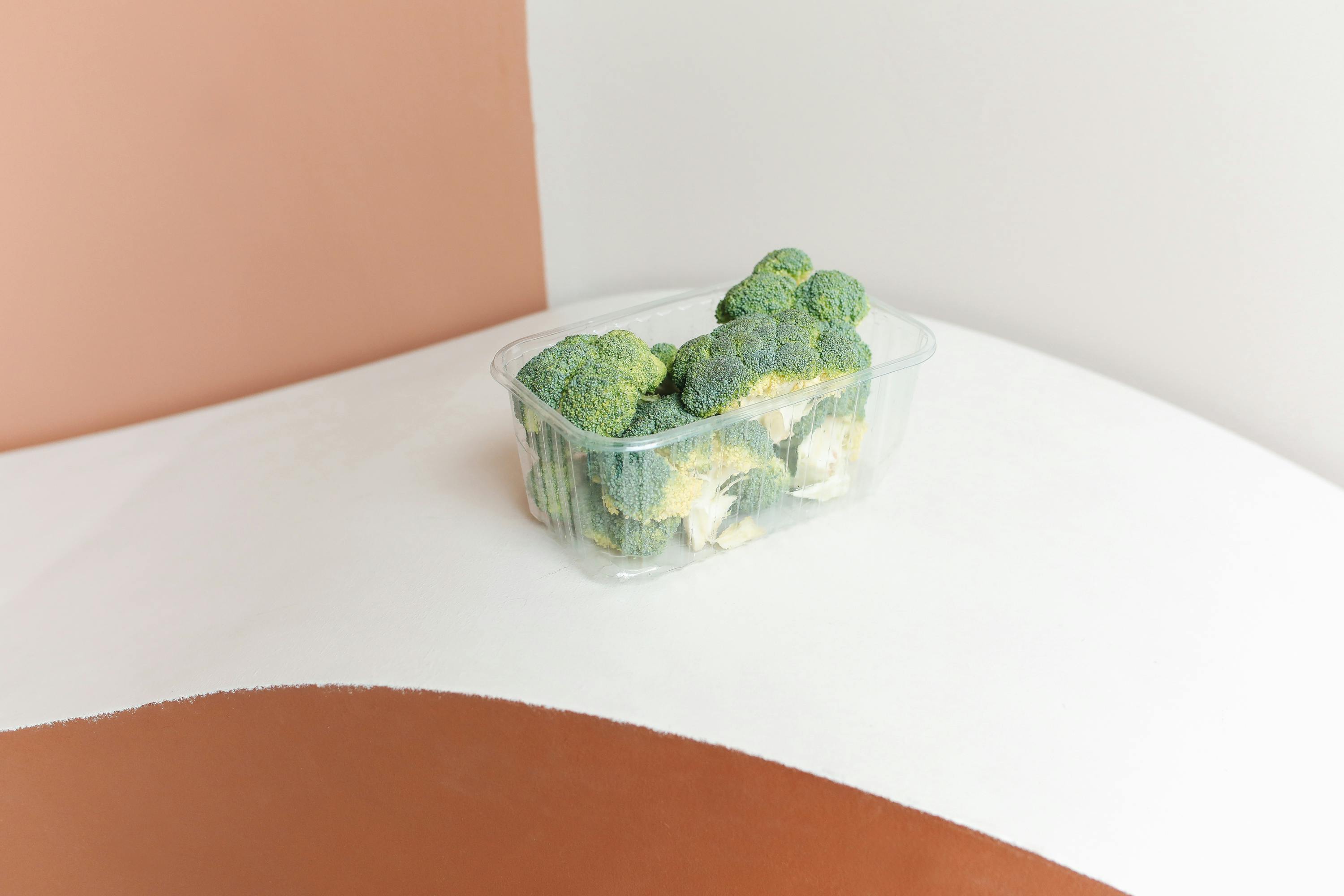 Minimalist photo of fresh broccoli in a plastic container on a modern backdrop.