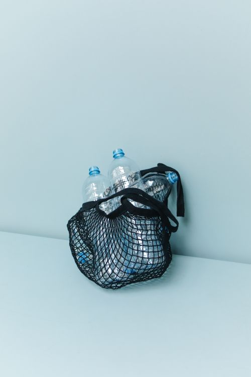 Free Sustainable black mesh bag filled with plastic bottles on pastel blue background. Stock Photo