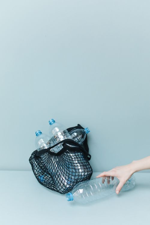 Free A hand reaching for plastic bottles in a net bag, promoting zero waste and recycling. Stock Photo