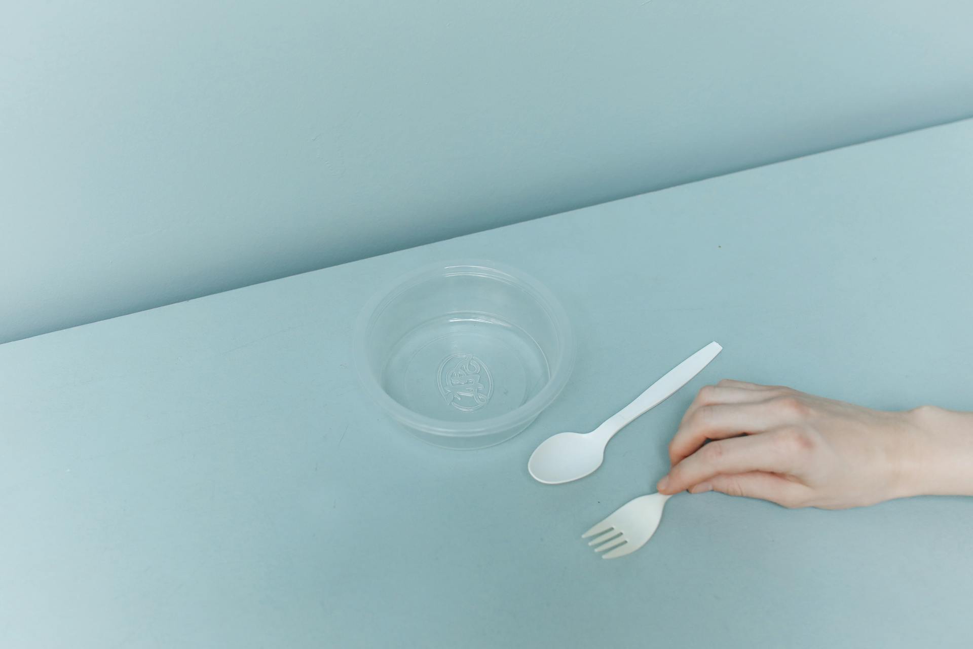 A minimalistic setup with plastic utensils and a container on a light blue surface for eco-friendly themes.