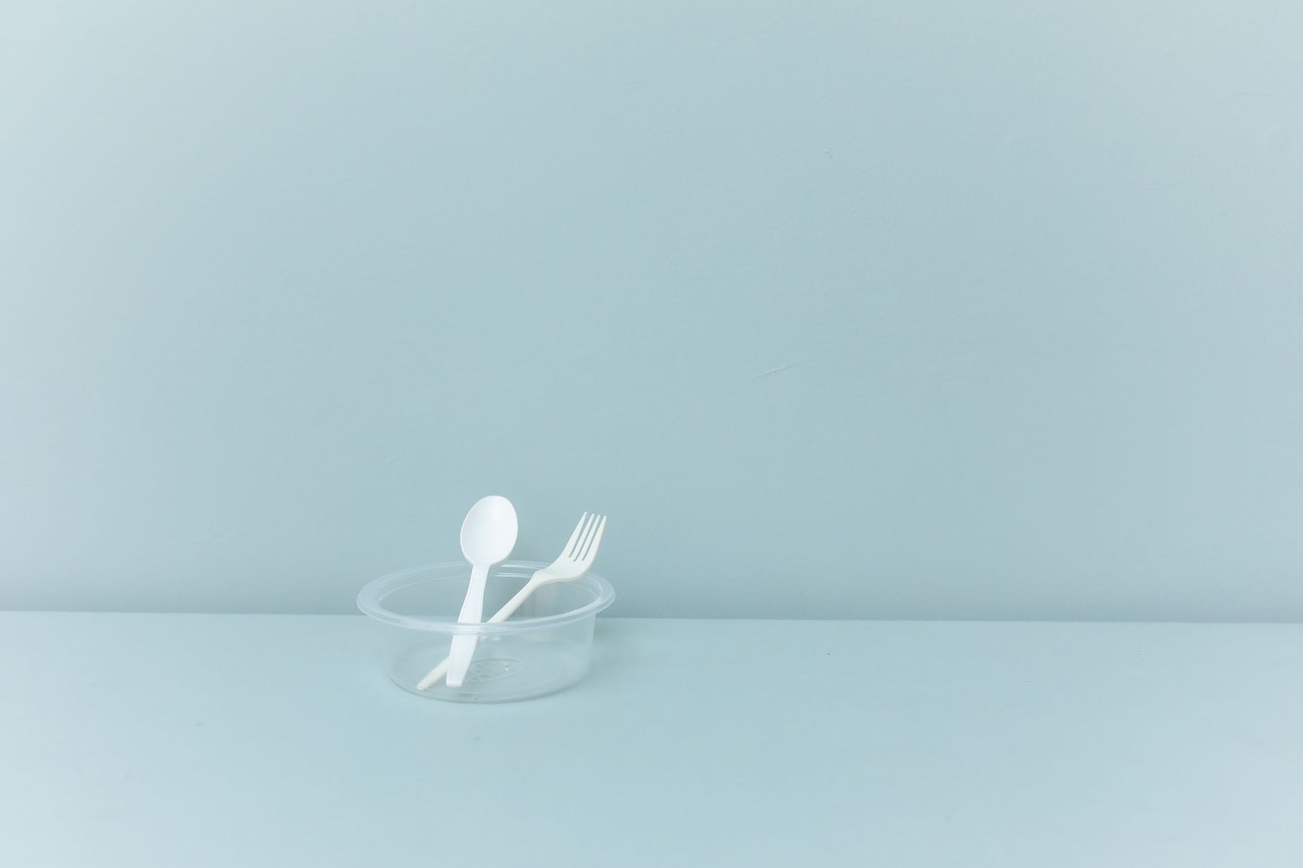 A minimalist still life featuring plastic cutlery in a container against a light blue background.