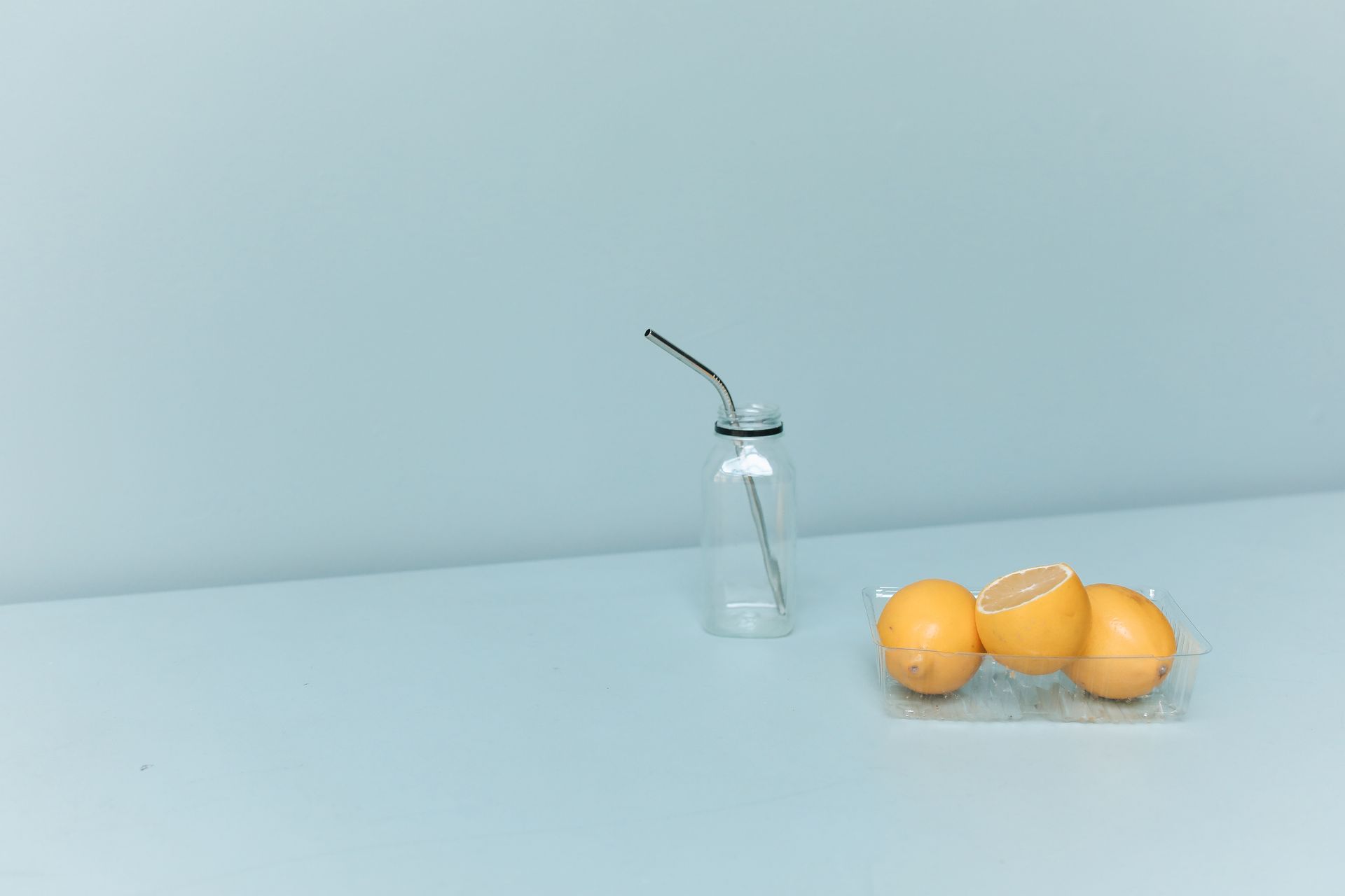 A minimalist still life showcasing a glass bottle with a metal straw and lemons.