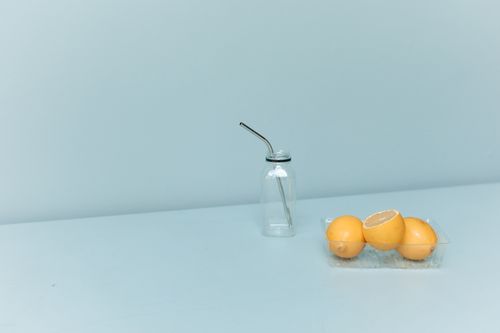 Free A minimalist still life showcasing a glass bottle with a metal straw and lemons. Stock Photo
