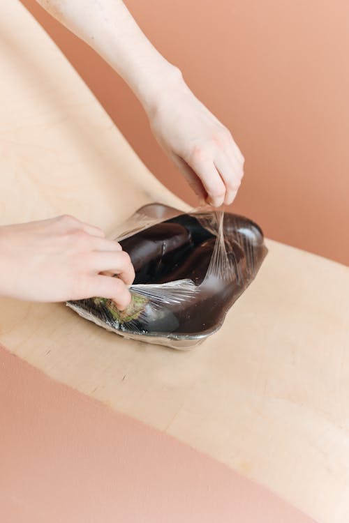 Person Opening Clear Plastic WIth Eggplants 