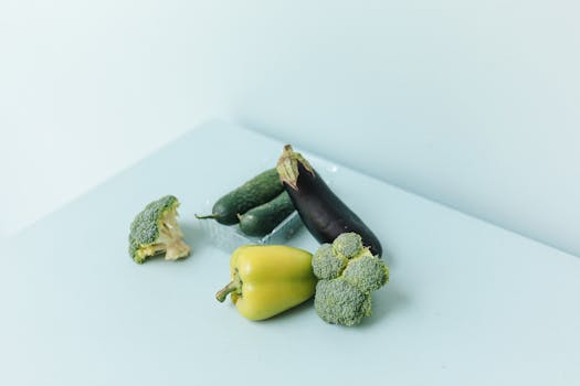 A fresh assortment of vegetables including broccoli, cucumber, and eggplant on a pastel background.