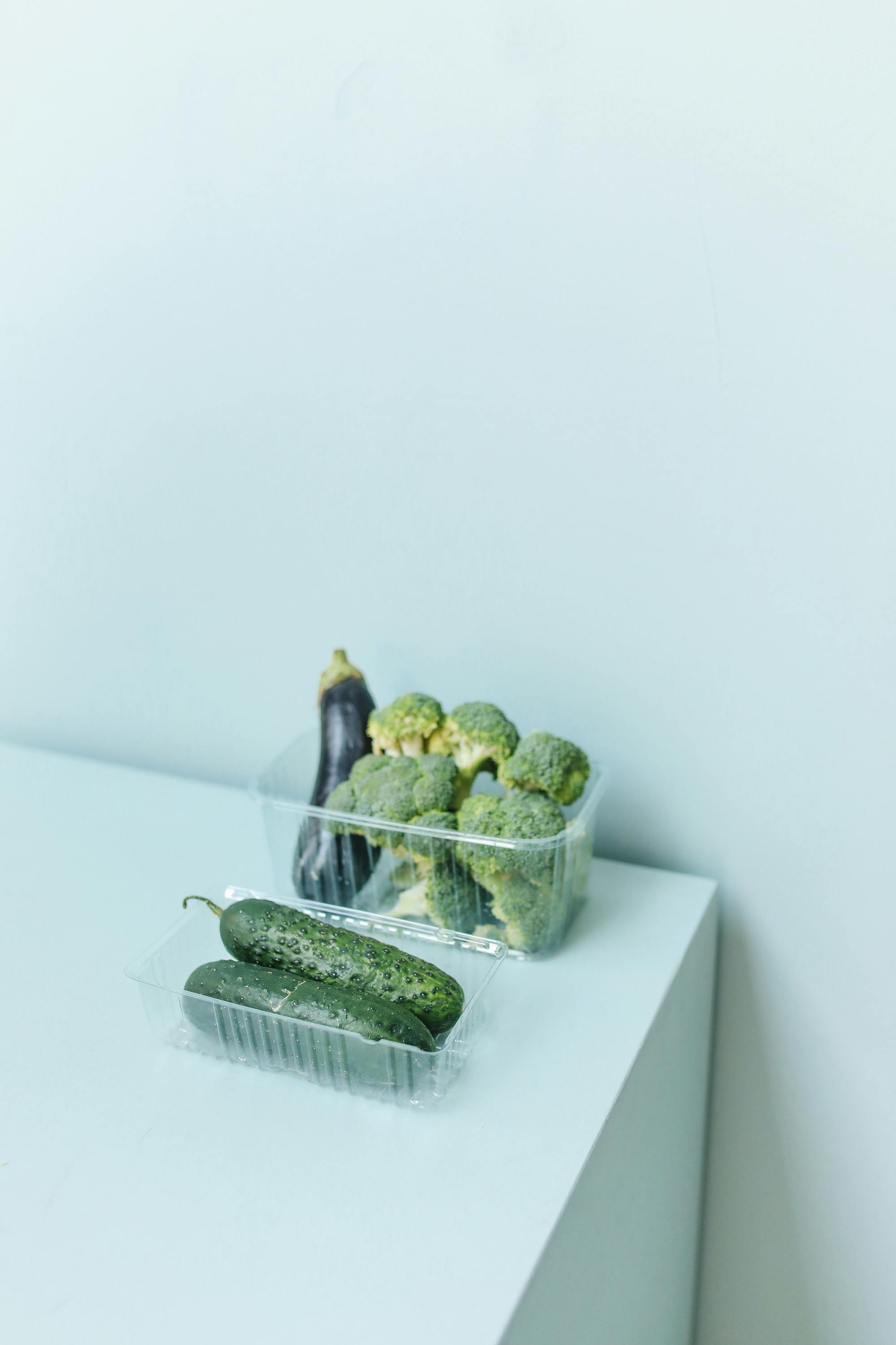 在干净的白色表面上，时尚地展示有机黄瓜和西兰花，完美诠释健康意识的生活