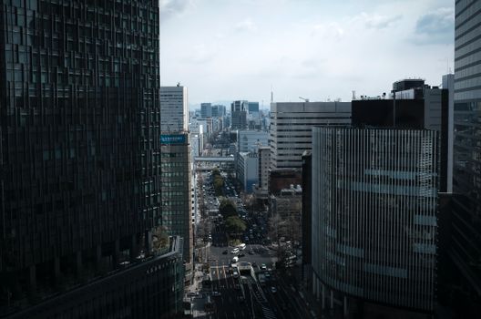 A bustling view of Nagoya's cityscape with tall buildings lining the streets on a cloudy day.