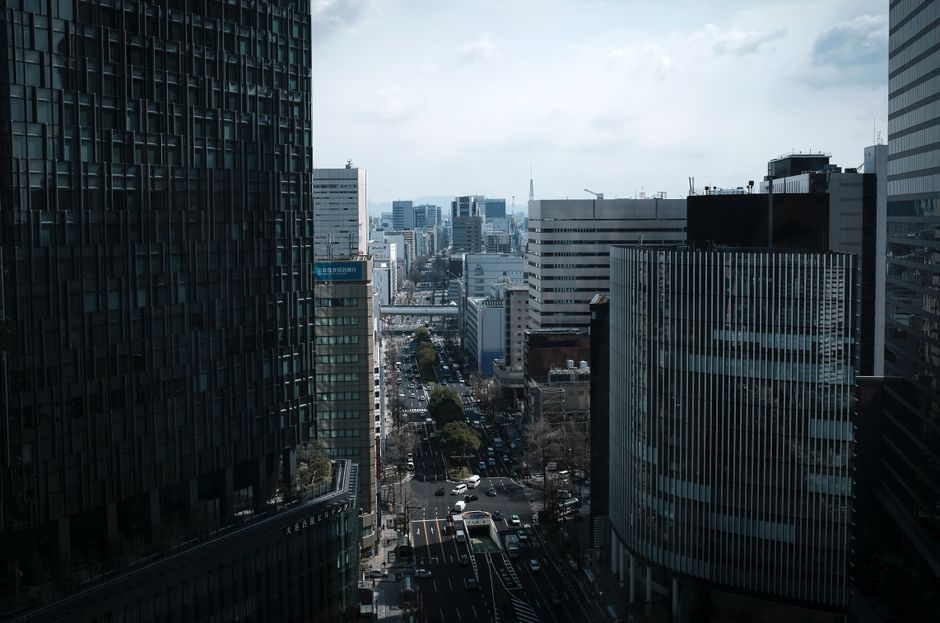 A bustling view of Nagoya's cityscape with tall buildings lining the streets on a cloudy day.