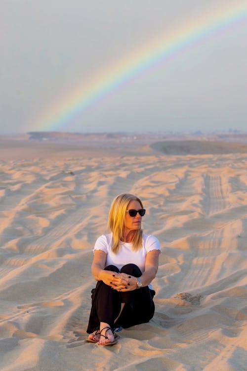 Woman in sandy desert under sky with rainbow