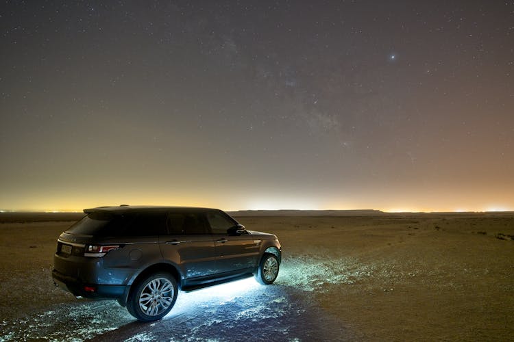 Car Driving On Sandy Desert In Evening Under Sky