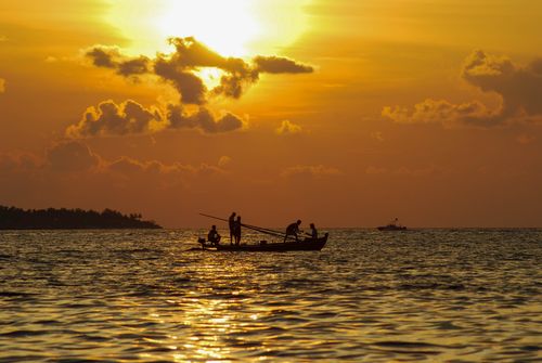 Free Silhouetted fishermen on a boat during a golden sea sunset in the Maldives. Stock Photo